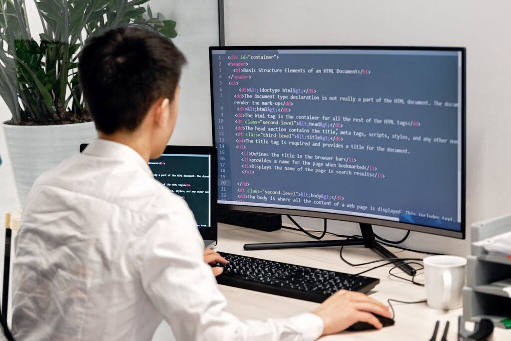 pexels photo 7988113 Adult male programmer coding on dual monitors in a modern indoor workspace.